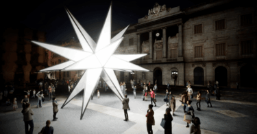 La plaza Sant Jaume se convierte este año en un verdadero epicentro de la Navidad en Barcelona, gracias a una propuesta innovadora que combina tradición e innovación. La instalación de una espectacular estrella luminosa de 20 puntas, llamada "Origen", será el centro de atención de la plaza, mientras que dos pesebres, situados en el interior del Ayuntamiento y del Palau de la Generalitat, complementarán la decoración navideña. Este proyecto, fruto de la colaboración entre el Ayuntamiento de Barcelona y la Generalitat de Catalunya, promete ofrecer una experiencia única para ciudadanos y visitantes. Una estrella monumental como símbolo de perfección La estrella "Origen" no es solo una pieza decorativa; es una obra de arte que destaca por su diseño y significado. Creada por Xevi Bayona y Àlex Posada, la estrella representa un icosaedro, una figura geométrica de 20 caras triangulares que simboliza perfección, armonía y equilibrio. Este diseño geométrico también evoca conceptos universales, como el momento germinal del universo, conocido como el Big Bang, cuando la oscuridad se transformó en luz y energía. Con un diámetro de nueve metros y un peso de 2,5 toneladas, la estrella está fabricada con hierro, metacrilato y tecnología LED, lo que garantiza tanto su durabilidad como su espectacularidad visual. Durante el día, esta obra se presenta como una imponente escultura geométrica en el lateral de la plaza, cerca de las calles Ferran y del Call. Sin embargo, es al anochecer cuando despliega todo su potencial: se convierte en un faro luminoso que proyecta reflejos de luz sobre las fachadas del Ayuntamiento y del Palau de la Generalitat. Además, la instalación cuenta con una banda sonora original que añade un componente sensorial al espectáculo, haciendo que la experiencia sea aún más inmersiva y cautivadora. Dos pesebres para honrar la tradición navideña La decoración de la plaza Sant Jaume no estaría completa sin los tradicionales pesebres, que este año se han trasladado al interior de los edificios históricos para enriquecer la experiencia de los visitantes. El Pati de Carruatges del Ayuntamiento acogerá el pesebre tradicional, elaborado por la Associació de Pessebristes. Este diorama incluirá referencias al centenario del poeta Joan Salvat-Papasseit, quien trabajó en el Moll de la Fusta, y a la reciente edición de la Copa América de vela en Barcelona. La exposición estará abierta al público del 29 de noviembre al 5 de enero, ofreciendo una oportunidad única para disfrutar de esta emblemática tradición en un entorno singular. Por su parte, el Palau de la Generalitat abrirá sus puertas entre el 14 y el 20 de diciembre para mostrar su decoración navideña. Los visitantes podrán descubrir un pesebre, un tió y avetos decorados, ambientados con un estilo que combina tradición y modernidad. Esta iniciativa no solo fomenta el espíritu navideño, sino que también permite a la ciudadanía explorar espacios habitualmente reservados. Colaboración entre instituciones para una Navidad especial El proyecto de decoración de la plaza Sant Jaume es el resultado de una estrecha colaboración entre el Ayuntamiento y la Generalitat, que han trabajado juntos para ofrecer una propuesta unificada y coherente. Ambas instituciones también han compartido la misma ornamentación vegetal en los balcones de sus edificios, reforzando la idea de cohesión. El coste total de la estrella luminosa asciende a 145.000 euros, mientras que el pesebre del Ayuntamiento ha supuesto una inversión adicional de 50.000 euros. Aunque el Ayuntamiento ha asumido la mayor parte del gasto, el concejal Jordi Marcé destacó la importancia de esta colaboración: "Estamos agradecidos de que la Generalitat nos haya apoyado en una iniciativa que siempre ha sido del Ayuntamiento. Esto refuerza el compromiso de ambas instituciones con la Navidad y con la ciudad de Barcelona." Una instalación con visión de futuro La estrella "Origen" no está concebida como una decoración efímera. Tanto el Ayuntamiento como la Generalitat han dejado abierta la posibilidad de reutilizar esta monumental pieza en futuras ediciones, consolidándola como un símbolo navideño de Barcelona. Este enfoque no solo busca maximizar el impacto de la inversión, sino también establecer un vínculo emocional con los ciudadanos, que podrán disfrutar de esta obra año tras año. Polémica y tradición en Sant Jaume La decoración navideña de la plaza Sant Jaume siempre ha sido objeto de debate, especialmente en torno a los pesebres. El traslado del pesebre al interior del Ayuntamiento y la Generalitat ha generado opiniones divididas, pero las instituciones han defendido la decisión como una forma de enriquecer la experiencia navideña. Según Marcé, "reubicamos las piezas para aprovechar al máximo el espacio y ofrecer una propuesta artística más completa." La estrella luminosa y los dos pesebres no solo buscan embellecer la plaza, sino también reforzar el mensaje de unidad y colaboración entre las instituciones. Además, el diseño y la ubicación de la estrella fueron seleccionados para resaltar el carácter icónico de Sant Jaume como punto de encuentro entre tradición e innovación. Sant Jaume, el corazón de la Navidad en Barcelona Con estas iniciativas, la plaza Sant Jaume se consolida como uno de los principales puntos de interés navideño en Barcelona. La combinación de una monumental estrella luminosa, dos pesebres emblemáticos y una decoración coherente en toda la plaza crea un entorno mágico que invita a barceloneses y turistas a sumergirse en el espíritu de las fiestas. Sant Jaume no solo es un espacio de celebración, sino también un símbolo de la capacidad de Barcelona para combinar tradición y modernidad, demostrando que la Navidad puede ser un momento para innovar sin perder de vista las raíces culturales de la ciudad.